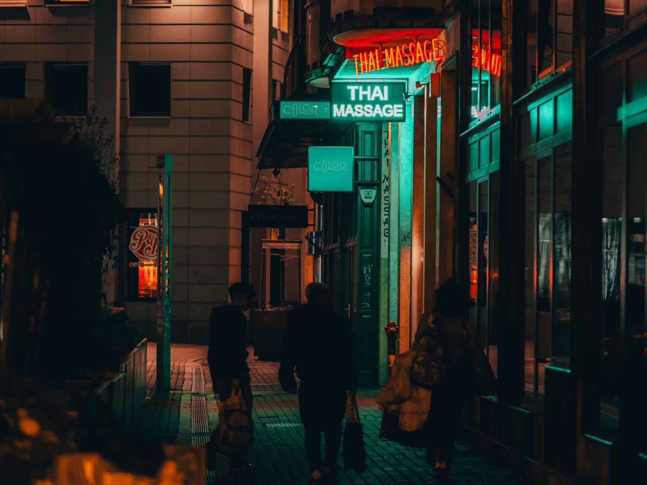 Moody nighttime street scene near a Thai massage parlor in Budapest, capturing urban life.